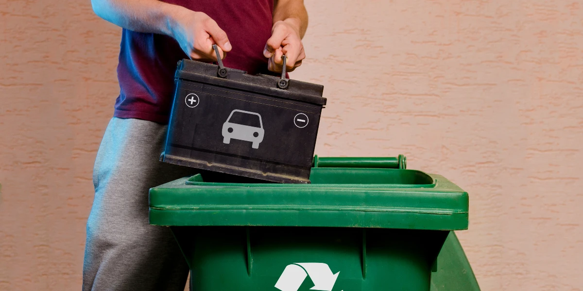 Recyclage d'une batterie de voiture dans une poubelle verte avec un symbole de recyclage